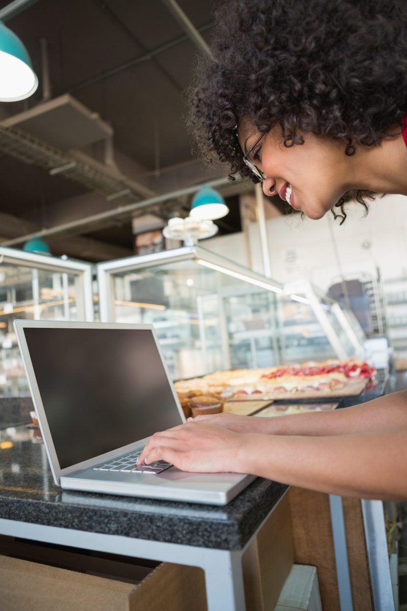 Pretty waitress smiling and using laptop at the bakery Pretty waitress smiling and using laptop at the bakery